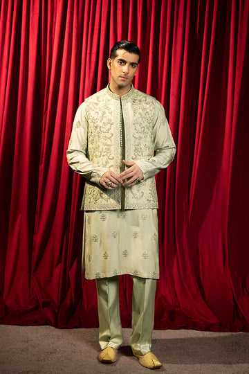 A pastel green waistcoat made from luxurious silk, intricately hand-embellished with Mughal floral patterns using matte sequins, tilla, resham, and cut dana thread-work. It is paired with a matching kurta and pajama set featuring a detailed floral neckline with an all-over motif, enhanced with sequins and resham embroidery.